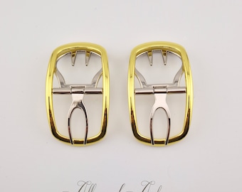 May include: Two gold-colored metal buckles with a silver-colored center mechanism. The buckles have a rectangular shape with rounded edges and a decorative design. The image includes the text "Allures d'Antan".