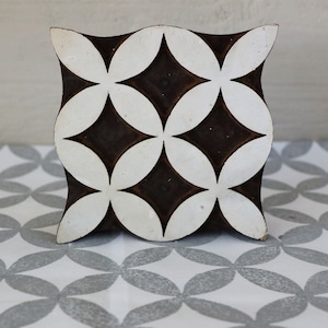 May include: A wooden block printing stamp with a geometric pattern of white circles and black diamonds. The stamp is designed to create a repeating pattern on fabric or paper.