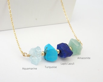 May include: A gold chain necklace featuring four raw gemstone beads separated by small gold spheres. The stones are labeled as Aquamarine, Turquoise, Lapis Lazuli, and Amazonite. The necklace has a delicate link design and a polished gold finish.