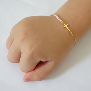 May include: A gold chain bracelet with a small gold cross charm and pink beads.