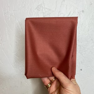 May include: A close-up of a rust-colored fabric swatch. The fabric is smooth and has a slight sheen.