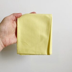 May include: A pale yellow fabric swatch. The fabric is smooth and has a slight sheen.