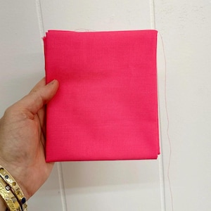 Könnte beinhalten: Ein hellrosa Stoffmuster. Der Stoff ist glatt und hat einen leichten Glanz.