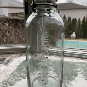May include: A clear glass jar with a wire bail closure. The jar is embossed with the text "JOS. W. MILLER, BY., INC."