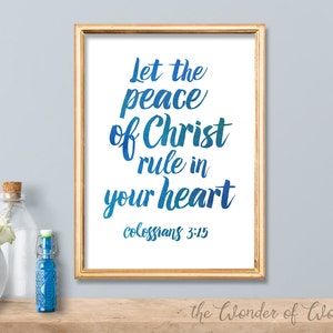 Puede incluir: Una impresión enmarcada con un texto degradado azul y verde que dice "Que la paz de Cristo reine en tu corazón" con la referencia bíblica "Colosenses 3:15" debajo. La impresión está enmarcada en un marco dorado y está sobre una superficie de madera.
