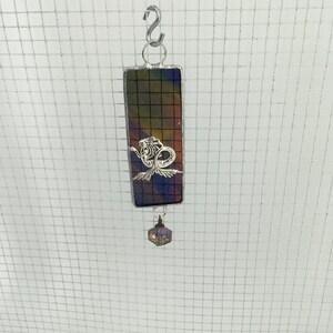 May include: A stained glass suncatcher featuring a mermaid design with a purple iridescent crystal hanging below. The suncatcher is framed in silver and has a dark background with shades of purple, blue, and green.