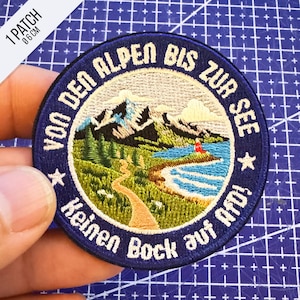 Könnte beinhalten: Ein runder, bestickter Aufnäher mit 6 cm Durchmesser, der eine Berglandschaft mit einem gewundenen Pfad und einem See zeigt. Der dunkelblaue Rand enthält den weißen Text 'VON DEN ALPEN BIS ZUR SEE' und 'Keinen Bock auf AfD' sowie zwei Sterne.
