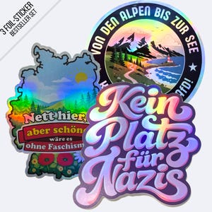 Könnte beinhalten: Ein Set aus drei holografischen Folienaufklebern. Ein Aufkleber ist geformt wie Deutschland mit dem Text 'Nett hier, aber schön wäre es ohne Faschismus'. Ein weiterer ist kreisförmig mit dem Text 'VON DEN ALPEN BIS ZUR SEE'. Der dritte zeigt den Text 'Kein Platz für Nazis'.