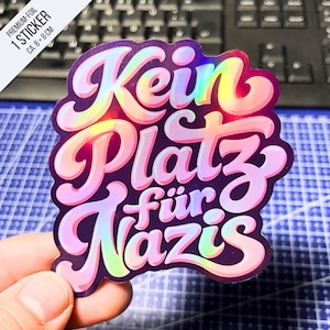Könnte beinhalten: Ein gestanzter Aufkleber mit dem Text "Kein Platz für Nazis" in einer fetten, abgerundeten, holografischen Schrift. Die Buchstaben zeigen ein wechselndes Spektrum irisierender Farben auf dunklem Hintergrund und messen ca. 8 cm x 8 cm.