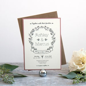 May include: A wedding invitation with a pink border and a floral wreath design. The invitation reads "Ashley & Marcus" and includes the date and time of the wedding. The text also says "Together with their families" and "Reception to follow".