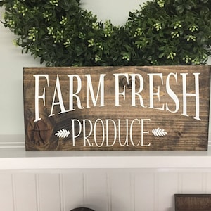 K&ouml;nnte beinhalten: Ein rustikales Holzschild mit dem Text "Farm Fresh Produce" in wei&szlig;en Buchstaben. Das Schild hat eine dunkelbraune Beize und einen Knoten im Holz.