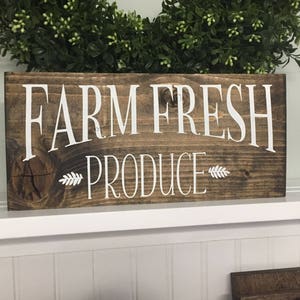 K&ouml;nnte beinhalten: Ein rustikales Holzschild mit dem Text "FARM FRESH PRODUCE" in wei&szlig;er Farbe. Das Schild hat eine braune Holzmaserung und ist perfekt f&uuml;r ein Bauernhaus oder eine Landhausk&uuml;che.