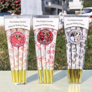 Puede incluir: Tres conos pre-enrollados en envases de plástico transparente. Cada cono presenta un diseño diferente: fresa, cereza y coco. El embalaje incluye el texto "Pre-Rolled Cones" y "Natural Rolling Paper". Los conos tienen puntas doradas.