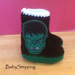 Op de afbeelding: Zwarte en groene gehaakte babyschoentjes met een groene en zwarte Hulk-applicatie.