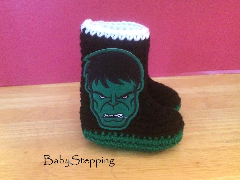 Op de afbeelding: Zwarte en groene gehaakte babyschoentjes met een groene en zwarte Hulk-applicatie.