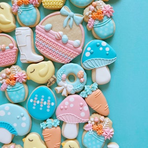 Op de afbeelding: Een verzameling paas-suikerkoekjes versierd met pastelkleuren en verschillende ontwerpen, waaronder kuikens, paddenstoelen, manden en bloemen.