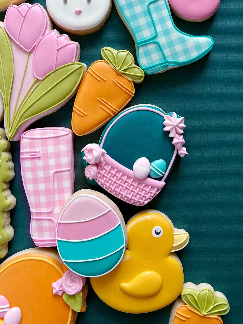 May include: A collection of Easter-themed sugar cookies decorated with colorful icing. The cookies feature a bunny, tulips, carrots, a duck, a basket, and rain boots.