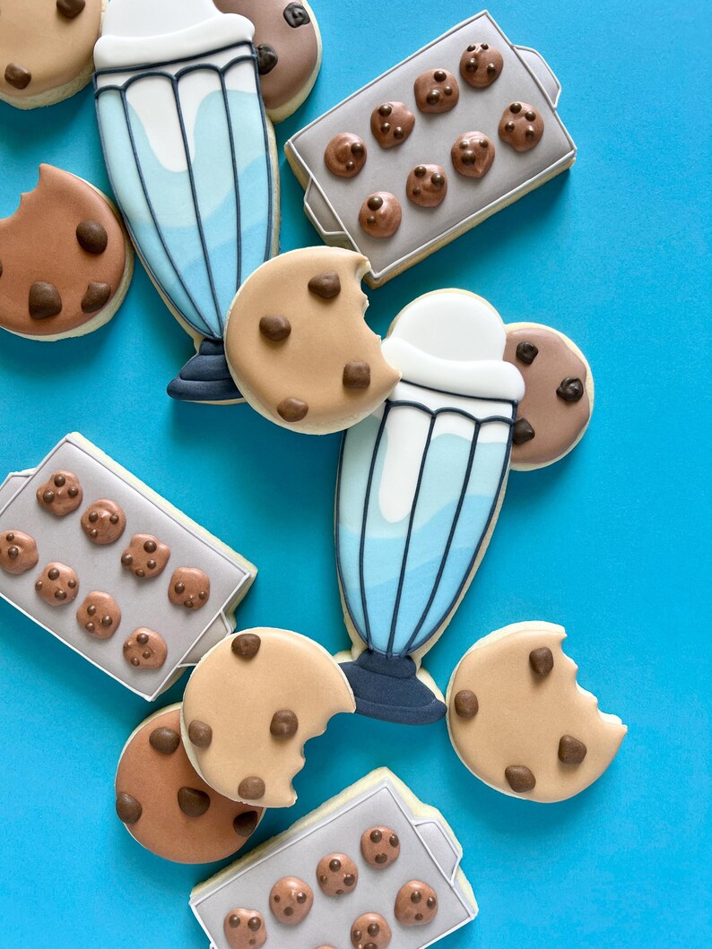 May include: An assortment of decorated sugar cookies on a bright blue surface. The cookies include chocolate chip cookies, some with a bite taken out, and milkshake-shaped cookies. There are also cookies shaped like baking trays with mini chocolate chip cookies.