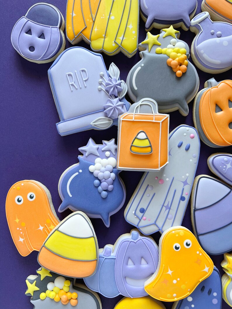 May include: A collection of Halloween-themed sugar cookies decorated with various designs, including ghosts, pumpkins, candy corn, a cauldron, a tombstone with the word "RIP" on it, and a shopping bag with a candy corn design.