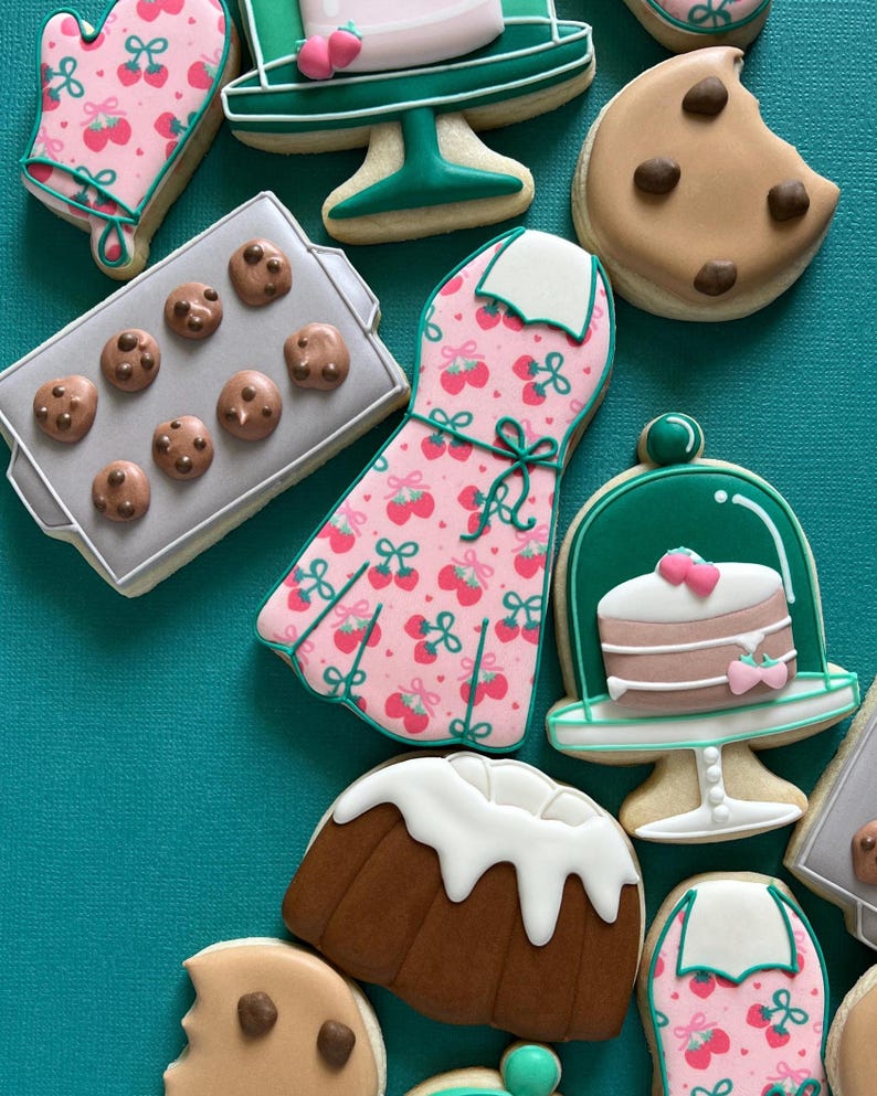 May include: Assortment of decorated sugar cookies in various shapes, including a dress, oven mitt, cake, and chocolate chip cookies. The cookies are decorated with pink, green, white, and brown icing, and arranged on a teal background.