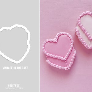 May include: Two pink heart-shaped cakes with a decorative piped border. The cakes are on a pink background. The text "Vintage Heart Cake" is below the cakes.