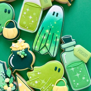 Puede incluir: Una colecci&oacute;n de galletas de az&uacute;car con tem&aacute;tica de Halloween decoradas con glaseado verde, amarillo y blanco. Las galletas representan fantasmas, sombreros de bruja, calderos y botellas de poci&oacute;n con las palabras "Poci&oacute;n" y "Veneno" en las etiquetas.