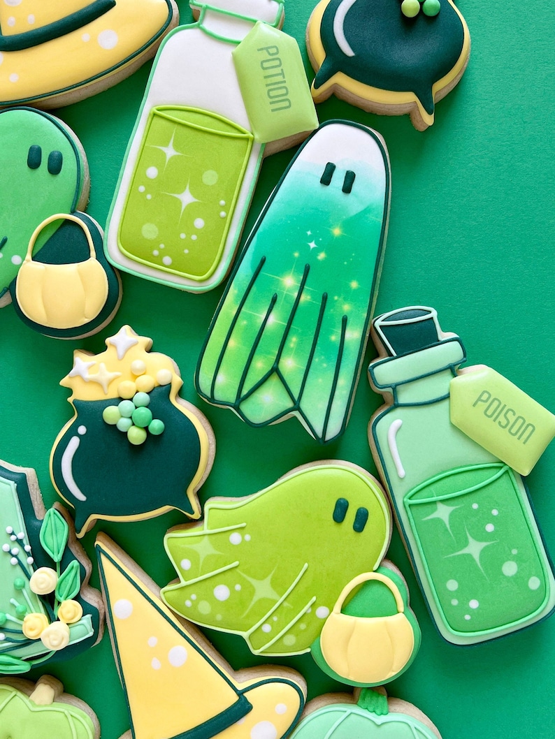 Puede incluir: Una colecci&oacute;n de galletas de az&uacute;car con tem&aacute;tica de Halloween decoradas con glaseado verde, amarillo y blanco. Las galletas representan fantasmas, sombreros de bruja, calderos y botellas de poci&oacute;n con las palabras "Poci&oacute;n" y "Veneno" en las etiquetas.