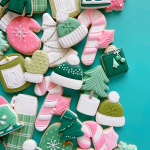 Pode incluir: Conjunto de biscoitos de a&ccedil;&uacute;car com tema natalino decorados com glac&ecirc; verde, rosa e branco. Os biscoitos apresentam desenhos como luvas, bengalas de doces, &aacute;rvores de Natal e chap&eacute;us. Alguns biscoitos t&ecirc;m a palavra "JOY" escrita neles.