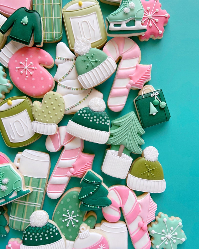 Pode incluir: Conjunto de biscoitos de a&ccedil;&uacute;car com tema natalino decorados com glac&ecirc; verde, rosa e branco. Os biscoitos apresentam desenhos como luvas, bengalas de doces, &aacute;rvores de Natal e chap&eacute;us. Alguns biscoitos t&ecirc;m a palavra "JOY" escrita neles.