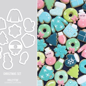 May include: A set of 12 Christmas cookie cutters in various shapes, including a snowman, a stocking, a Christmas tree, a present, a snowflake, a mitten, a light bulb, a donut, a mug, a sweater, a candy cane, and a wreath. The cutters are made of white metal and are arranged on a grey background. The text "CHRISTMAS SET" and "HOLLY FOX COOKIE CUTTERS" is printed below the cutters.