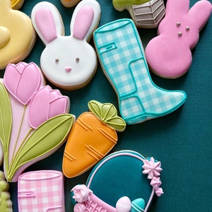 May include: Assortment of Easter-themed sugar cookies decorated with colorful icing.  The cookies include a bunny, a carrot, a tulip, a rain boot, a basket, and a chick.