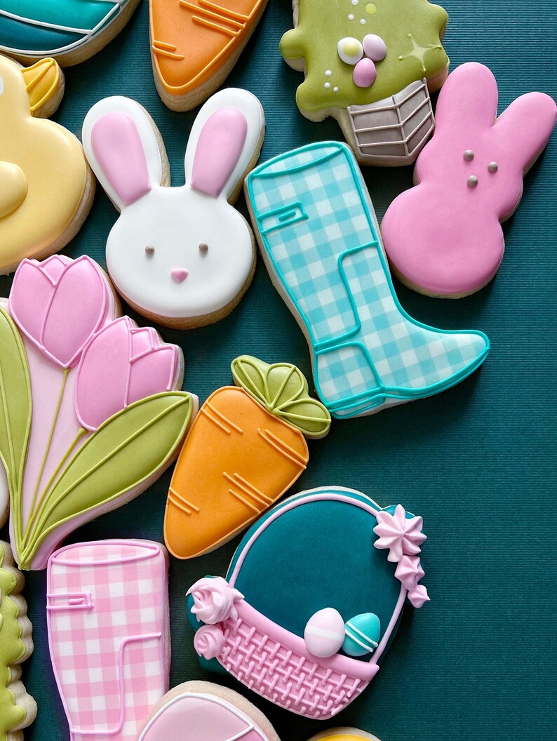 May include: Assortment of Easter-themed sugar cookies decorated with colorful icing.  The cookies include a bunny, a carrot, a tulip, a rain boot, a basket, and a chick.