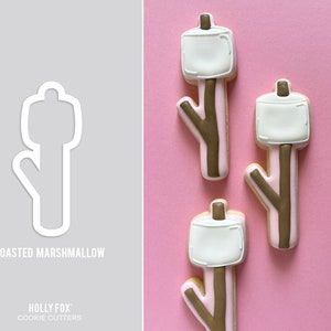 May include: Three brown and white cookie cutters shaped like roasted marshmallows on sticks. The cookie cutters are on a pink background. The text "ROASTED MARSHMALLOW" is at the bottom of the image.