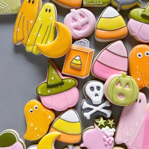 May include: A collection of Halloween-themed sugar cookies decorated with various designs, including ghosts, pumpkins, candy corn, and a witch's hat. The cookies are all different colors, including pink, yellow, orange, green, and white.
