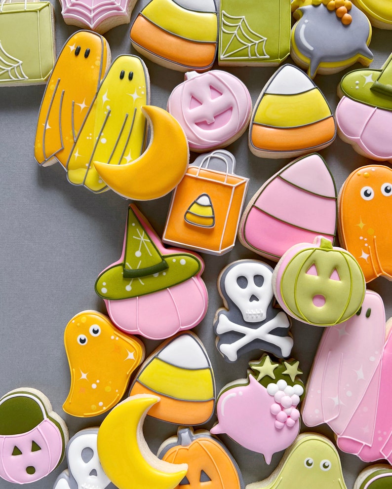 May include: A collection of Halloween-themed sugar cookies decorated with various designs, including ghosts, pumpkins, candy corn, and a witch's hat. The cookies are all different colors, including pink, yellow, orange, green, and white.
