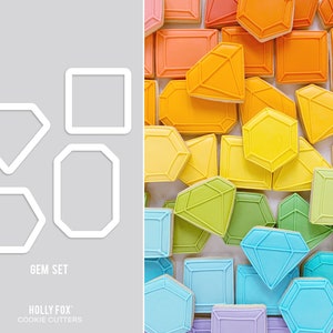 May include: A set of four cookie cutters shaped like different gemstones. The cutters are shown against a gray background. The cutters are labeled "Gem Set" and "Holly Fox Cookie Cutters".