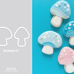 May include: A set of four cookie cutters shaped like mushrooms. The cutters are in the shape of a mushroom with a cap and a stem. The cutters are white and are arranged in a row on a gray background. The text "MUSHROOM SET" is below the cutters. The text "HOLLY FOX" is below the text "MUSHROOM SET". The text "COOKIE CUTTERS" is below the text "HOLLY FOX".