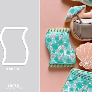 May include: A cookie cutter shaped like a beach towel, with the text "BEACH TOWEL" below it. The image also shows decorated cookies, including a beach towel cookie with a floral pattern in teal and pink.