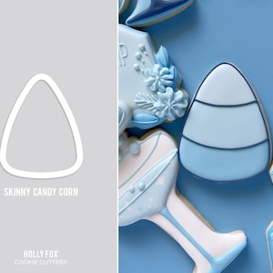 Puede incluir: Un cortador de galletas blanco con forma de ma&iacute;z de caramelo delgado. El cortador de galletas est&aacute; sobre un fondo gris. El texto "Skinny Candy Corn" est&aacute; debajo del cortador de galletas. El texto "Holly Fox Cookie Cutters" est&aacute; en la parte inferior de la imagen.