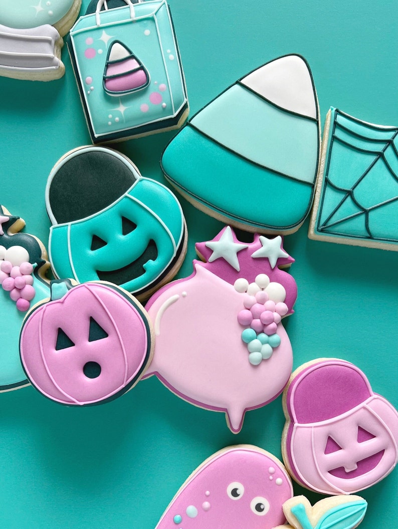 May include: Assortment of Halloween-themed sugar cookies decorated with teal, pink, and white icing. The cookies feature various designs, including pumpkins, ghosts, candy corn, and a shopping bag.