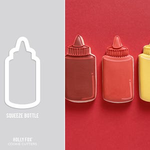 May include: Three squeeze bottle-shaped cookies, one brown, one red, and one yellow, arranged on a red background. The cookies have white outlines and detailed tops. A cookie cutter with the text "SQUEEZE BOTTLE" is on the left.