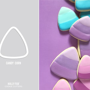 May include: Candy corn cookie cutters, a set of three, in the shape of a candy corn. The cutters are white and are shown on a gray background. The cutters are shown next to a purple background with several cookies decorated to look like candy corn.