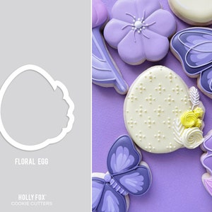 May include: A white cookie cutter in the shape of an egg with a floral design around the top. The cookie cutter is on a gray background. The text "Floral Egg" is below the cookie cutter. The text "HOLLY FOX" and "COOKIE CUTTERS" is below the text "Floral Egg".