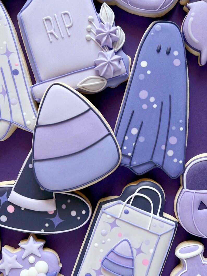 Puede incluir: Galletas de az&uacute;car de Halloween de color morado y blanco decoradas con varios dise&ntilde;os, incluyendo un fantasma, una l&aacute;pida con la palabra "RIP", un sombrero de bruja, un ma&iacute;z dulce, una bolsa de compras y una calabaza.