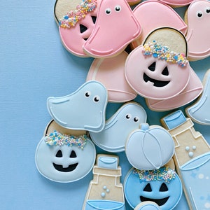 May include: A collection of Halloween-themed sugar cookies decorated with blue and pink frosting. The cookies are shaped like ghosts, pumpkins, and trick-or-treat bags. Some cookies have sprinkles on top.