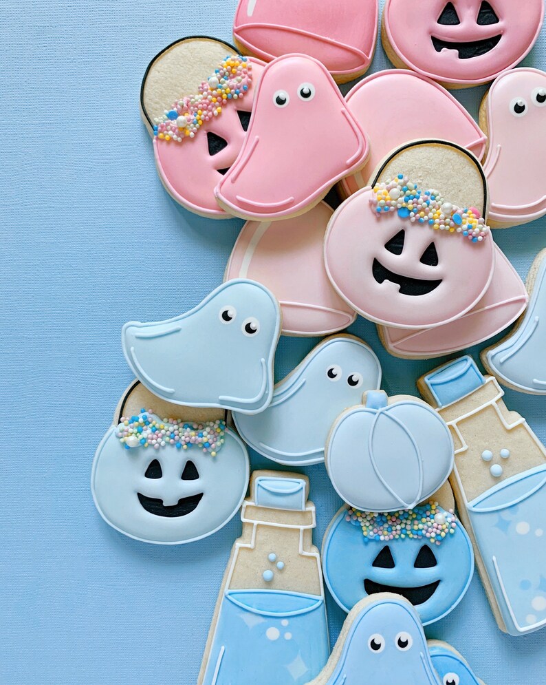 May include: A collection of Halloween-themed sugar cookies decorated with blue and pink frosting. The cookies are shaped like ghosts, pumpkins, and trick-or-treat bags. Some cookies have sprinkles on top.