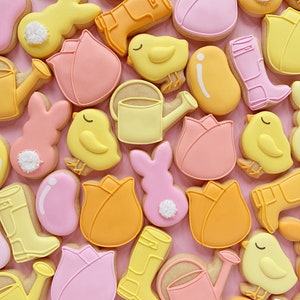 May include: A collection of spring-themed sugar cookies decorated with various designs, including tulips, chicks, bunnies, rain boots, and watering cans. The cookies are decorated in pastel colors, including pink, yellow, and orange.