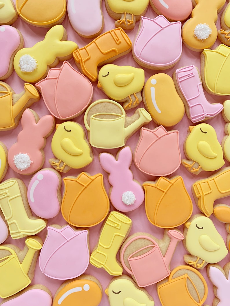 May include: A collection of spring-themed sugar cookies decorated with various designs, including tulips, chicks, bunnies, rain boots, and watering cans. The cookies are decorated in pastel colors, including pink, yellow, and orange.
