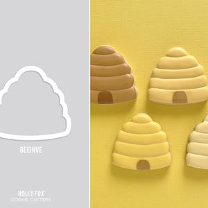 May include: A white outline of a beehive cookie cutter next to four beehive-shaped cookies. The cookies are various shades of yellow and brown, with a small brown entrance. The text "BEEHIVE" and "HOLLY FOX COOKIE CUTTERS" are also visible.