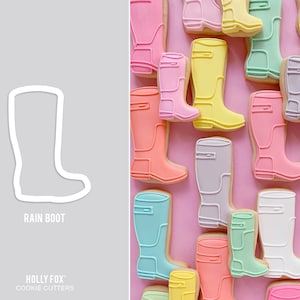 May include: A set of colorful rain boot cookie cutters. The cutters are in various colors, including pink, blue, yellow, and green. The cutters are arranged in a row on a pink background. The text "RAIN BOOT" is printed below the cutters.